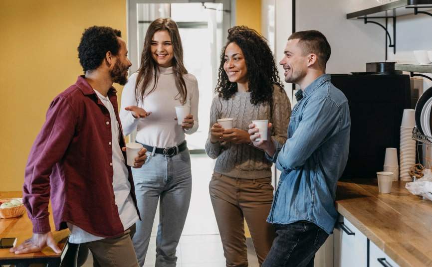 Four colleagues chatting and smiling over coffee in an office kitchen