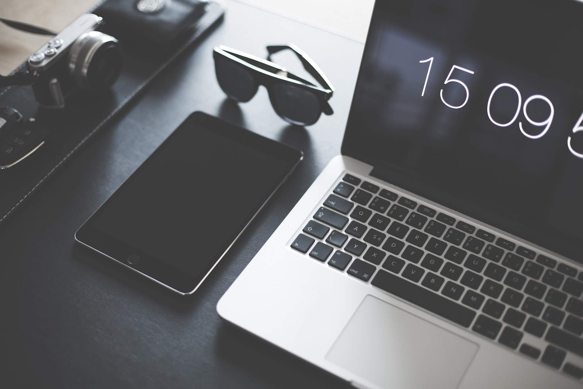A laptop, a tablet and sunglasses on a dark desk